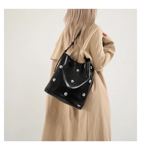 Detail of black bucket bag with silver studs worn over a classic khaki trench coat