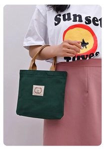 Detail of dark green canvas tote featuring bear embroidery and brown woven handles