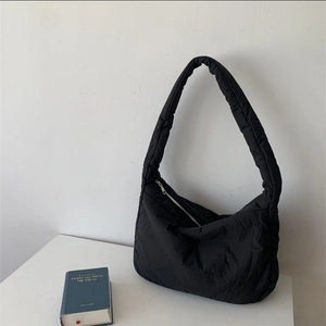 Detail of a soft black quilted puffer tote bag with zipper and padded strap on a white desk