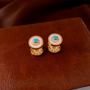 Macro shot of gold sunburst earrings with turquoise and zircon on leather