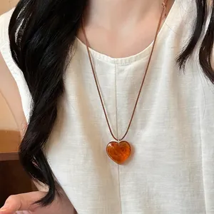 Detail of amber heart resin pendant with brown cord necklace on model wearing linen cloth