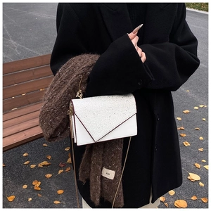 Nahaufnahme einer weißen Glitzer-Umschlagtasche mit einem braunen Strickschal