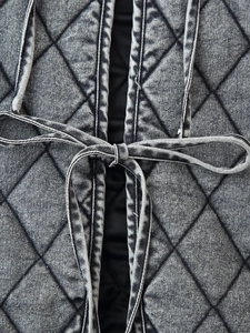 Detail of washed denim diamond quilted jacket showing thin tie-front bow and fabric texture