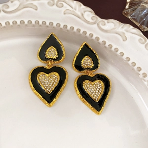 Detail of vintage black enamel heart earrings with crystals on a white embossed plate