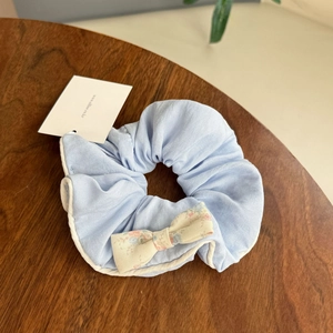 Light blue floral bow scrunchie with soft fabric texture on a warm wooden background