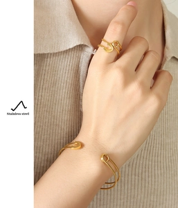 Detail of gold stainless steel safety pin open bracelet and ring set on model wrist