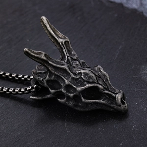 Vintage stainless steel dragon head skull pendant on a textured dark stone background