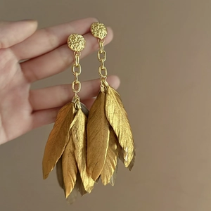 Detail of gold feather tassel earrings with hammered texture and long metallic chains