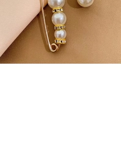 Detailed close-up of a gold pearl brooch pin with sparkling rhinestones on fabric