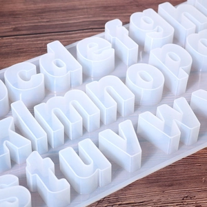 Detail of white silicone lowercase letter molds for resin on a dark wood background