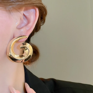 Detailed macro shot of large gold spiral earrings worn with a chic black suit