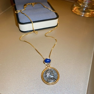 Detail of vintage gold necklace with blue oval stone and Greek coin pendant in a jewelry box