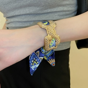 Close-up of vintage gold metal cuff bracelet wrapped in bohemian floral silk scarf on wrist