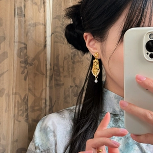 Close-up of golden geometric hollow pearl earrings shown on a model in vintage style