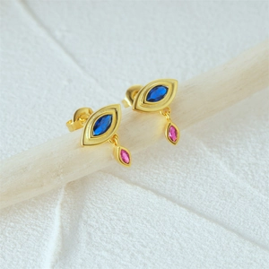 Close-up of gold Evil Eye earrings with blue stones and pink crystals on wood