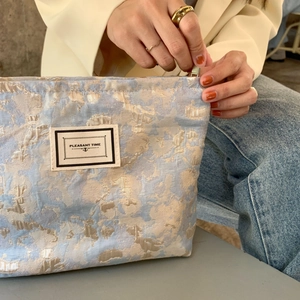 Detail of blue brocade cosmetic bag showing golden floral texture and PLEASANT TIME label