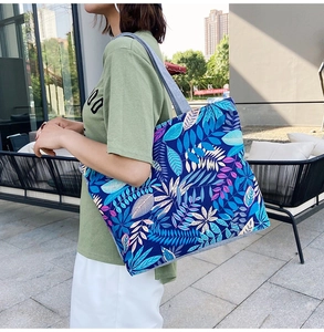 Short-haired woman carrying large tote bag with blue and purple leaf print in a cafe setting