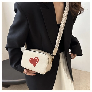 Detail of off-white crossbody bag with red heart and woven geometric strap on a model