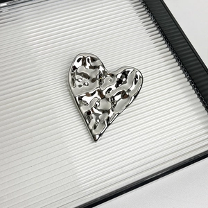 Close-up of heart-shaped silver brooch with irregular metallic texture on a tray