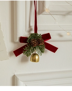 Close-up of red velvet bow with green pine needles, cones and golden bell ornament