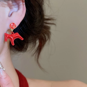 Close-up of red enamel Fu character earring on ear with gold Chinese lucky charm
