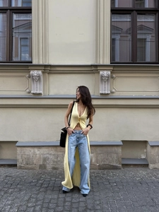 Close-up of a long pale yellow knitted vest paired with light blue straight jeans