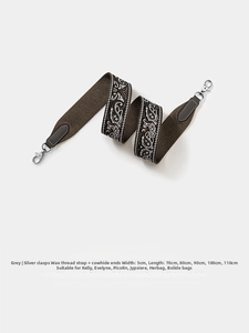 Close-up of wide woven bag strap with white floral pattern and silver metal clips