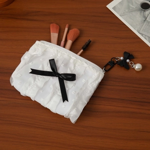 Close-up of white pleated cosmetic bag with black lace bow and pearl pendant detail