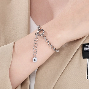 Detail of silver stainless steel chain bracelet featuring a round pendant with letter E