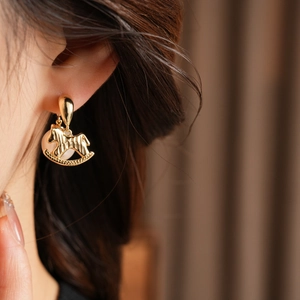 Gros plan de boucles d'oreilles cheval à bascule doré avec perle sur un mannequin