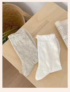 Detail of grey and white cotton socks with cute bow jacquard and ribbed cuffs on wood