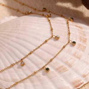 Detail of 18K gold-plated necklaces with green and white zircon on a white seashell