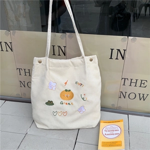 Gros plan d'un sac cabas en velours côtelé crème avec broderies de fruits et d'ours