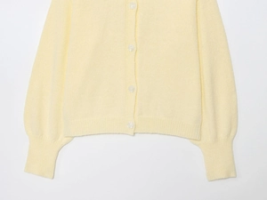 Close-up of pale yellow knit cardigan with delicate texture and white translucent buttons