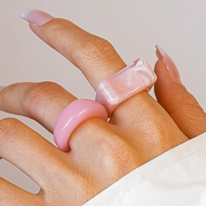 Macro view of pink marble pattern acrylic geometric square and round ring set on fingers