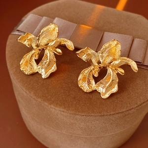 Detailed close-up of gold metal iris flower earrings on a brown velvet jewelry box