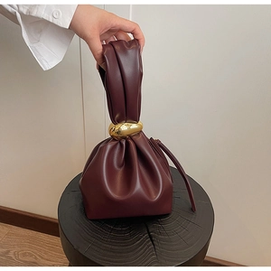 Close-up of burgundy pleated bucket bag with gold oval metal ring handle detail