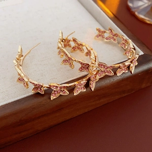 Détails des boucles d'oreilles créoles dorées avec motifs papillons et cristaux roses
