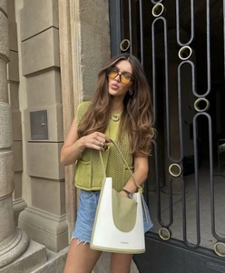 Detail view of a green knit vest paired with a white brand logo handbag on the street