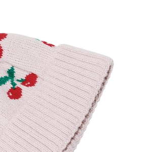 Close-up of pink knit winter hat featuring red cherry patterns and ribbed edge detail