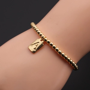 Gros plan d'un bracelet à perles dorées avec un pendentif rectangulaire lettre A