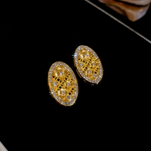 Dettaglio ravvicinato di orecchini ovali dorati vintage con trama traforata e cristalli