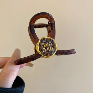 Detailed close-up of brown leopard print hair claw clip with golden brand logo element