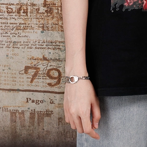 Detail of silver handcuff-style Cuban link bracelet on wrist with retro urban background