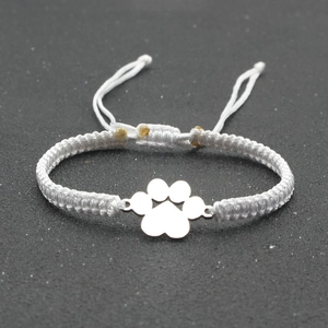 Close-up of handmade white braided lucky bracelet with silver dog paw print charm