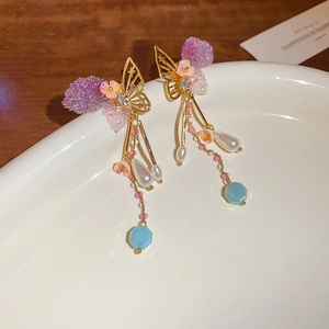Detail of butterfly fringe earrings with pearls on a white plate and wood background