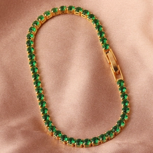 Detail of emerald green square zircon gold bracelet on beige silk background
