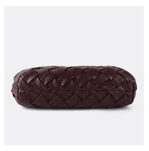 Detail view of the woven leather bottom of a dark red croissant bag with intricate texture