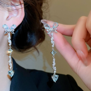 Macro detail of long tassel earrings with butterfly heart charms and blue zircons