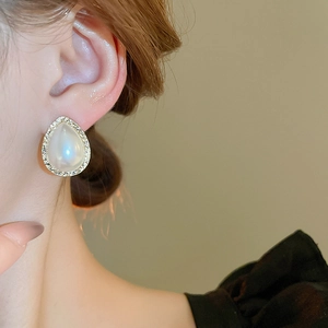 Elegant teardrop pearl earrings with diamond-encrusted edges worn by a model in soft light
